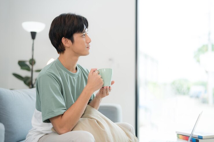 明るいリビングで朝のコーヒーを楽しんでいる若い男