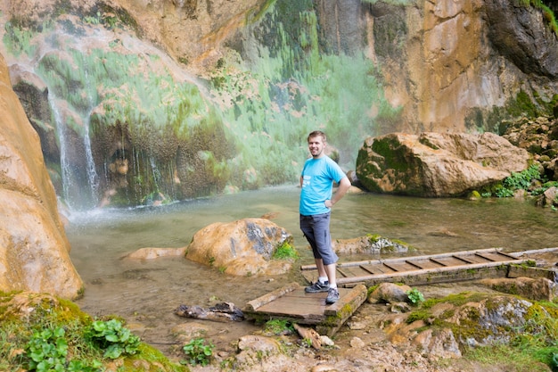 Young man enjoying in natural park at the base of large waterfall