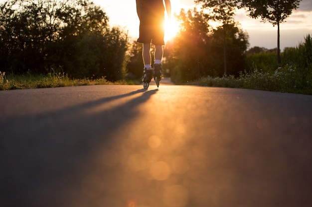 素敵な夏の日没時に自転車道でローラースケートを楽しんでいる若い男