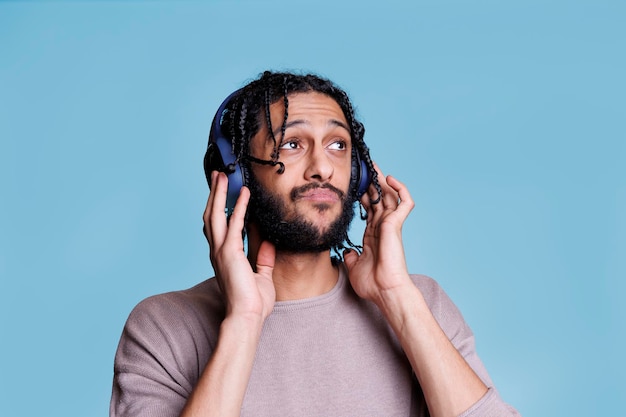 Young man enjoying song in wireless big headphones, pleased with playlist. Arab person listening to music in earphones with pensive facial expression while checking sound quality