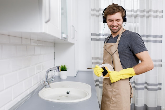 젊은 남자는 설거지하는 동안 음악을 즐긴다