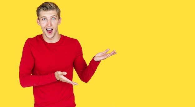 Young man of European appearance on a yellow background. directs two hands to an empty space. Joy and a smile on your face