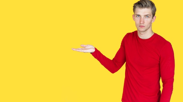 Young man of European appearance on a yellow background. holds one empty palm. Copy space