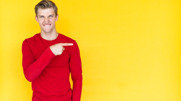 Young man of European appearance on a yellow background. the index finger points to an empty space. Copy space