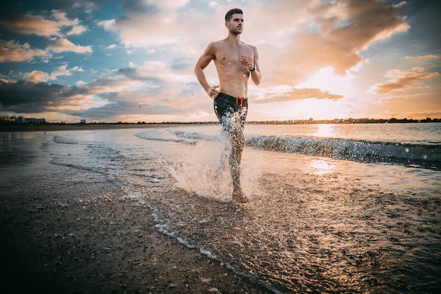 Foto un giovane uomo esercita sulla spiaggia al tramonto su una spiaggia. colori caldi