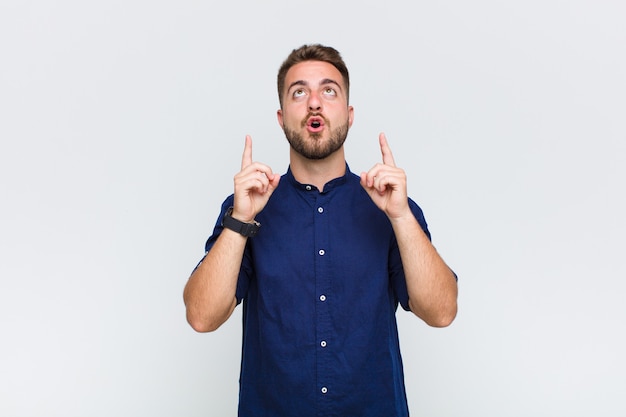 Young man feeling awed and open mouthed pointing upwards with a shocked and surprised look