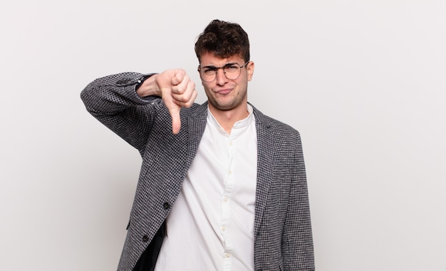 Young man feeling cross, angry, annoyed, disappointed or displeased, showing thumbs down with a serious look