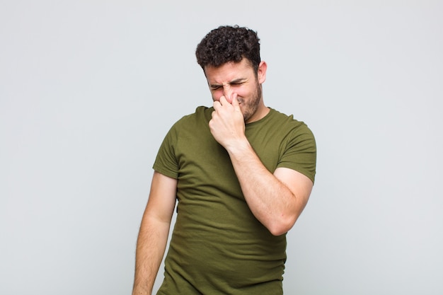 Young man feeling disgusted, holding nose to avoid smelling a foul and unpleasant stench