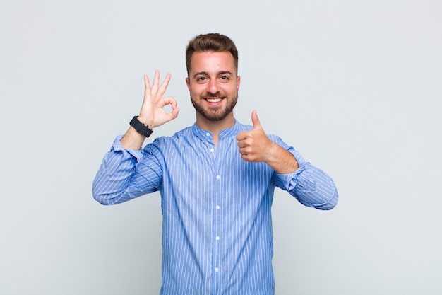 Giovane uomo che si sente felice, stupito, soddisfatto e sorpreso, mostrando i gesti ok e il pollice in alto, sorridente