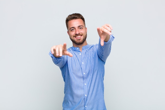 Young man feeling happy and confident, pointing to camera with both hands and laughing, choosing you