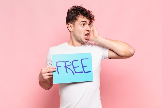 Young man feeling happy, excited and surprised, looking to the side with both hands on face