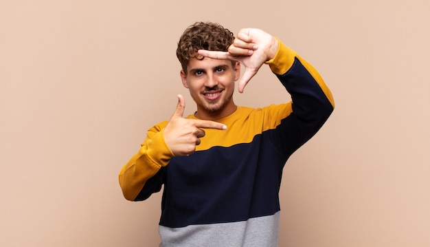 Young man feeling happy, friendly and positive, smiling and making a portrait or photo frame with hands