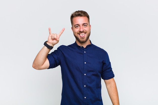 Young man feeling happy, fun, confident, positive and rebellious, making rock or heavy metal sign with hand