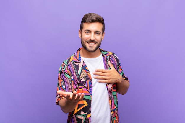 Young man feeling happy and in love, smiling with one hand next to heart and the other stretched up front