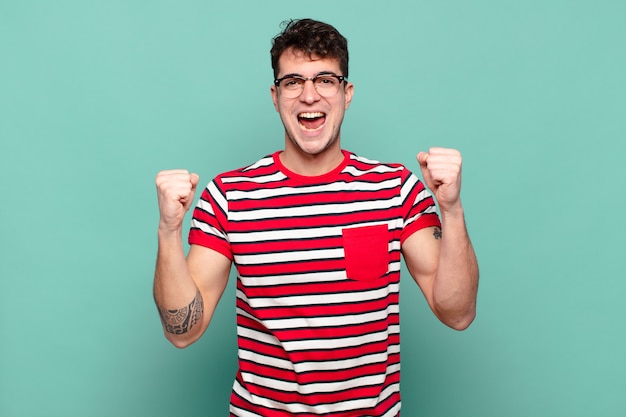 Young man feeling happy, positive and successful, celebrating victory, achievements or good luck