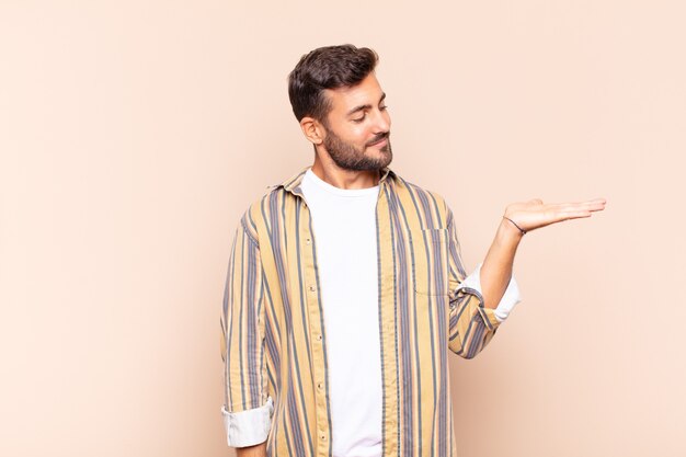 Young man feeling happy and smiling casually, looking to an object or concept held on the hand on the side