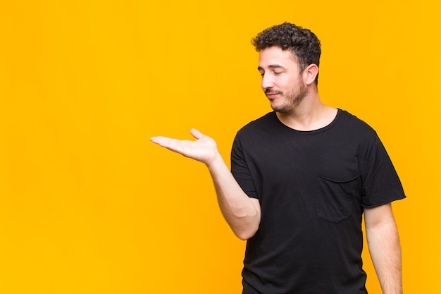 Young man feeling happy and smiling casually, looking to an object or concept held on the hand on the side