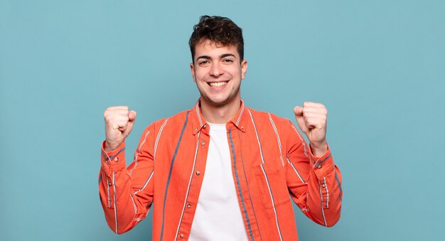 Young man feeling happy, surprised and proud, shouting and celebrating success with a big smile