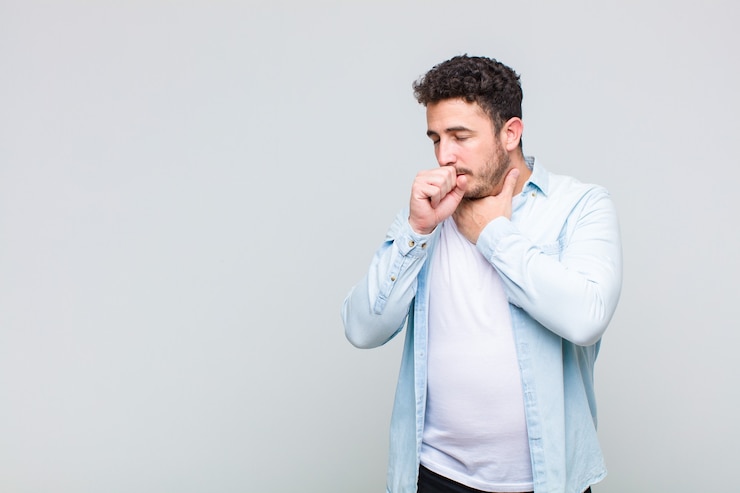 Photo young man feeling ill with a sore throat and flu symptoms, coughing with mouth covered