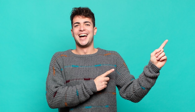 Young man feeling joyful and surprised, smiling with a shocked expression and pointing to the side