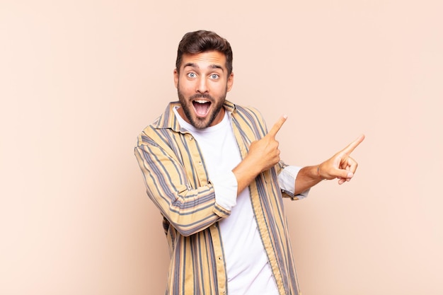 Young man feeling joyful and surprised smiling with a shocked expression and pointing to the side