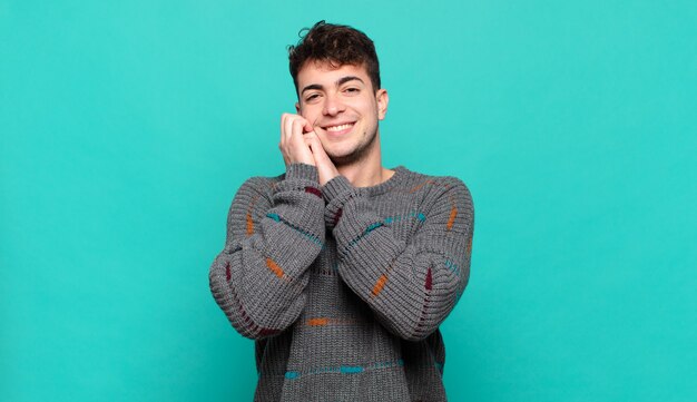 Young man feeling in love and looking cute, adorable and happy, smiling romantically with hands next to face