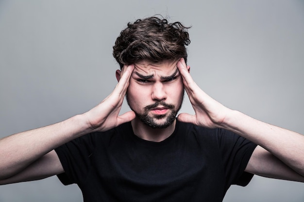 Young man feeling pain frowning with hand on head with gray background