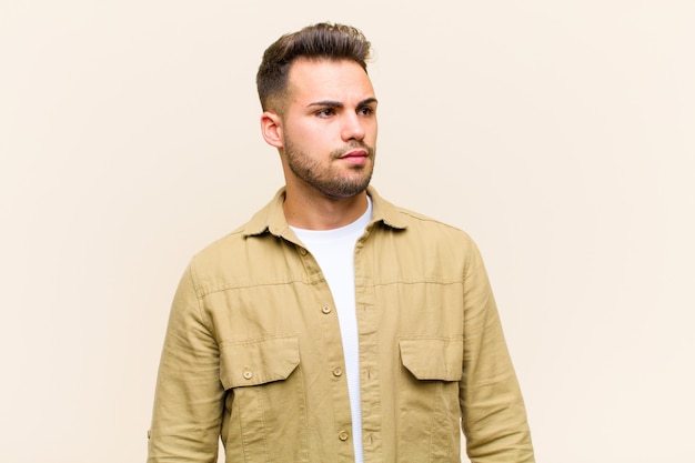 Young  man feeling sad, upset or angry and looking to the side with a negative attitude, frowning in disagreement against isolated background