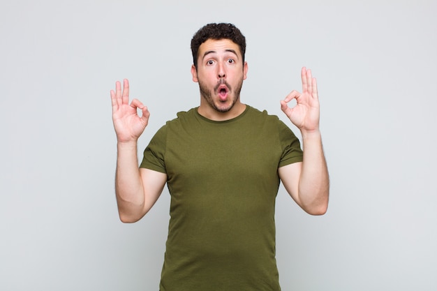 Young man feeling shocked, amazed and surprised, showing approval making okay sign with both hands