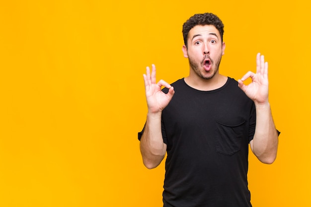 Young man feeling shocked, amazed and surprised, showing approval making okay sign with both hands