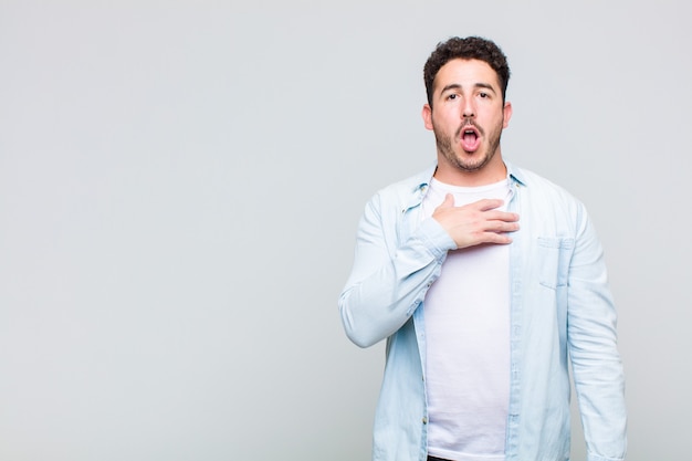 Young man feeling shocked, astonished and surprised, with hand on chest and open mouth, saying who, me?