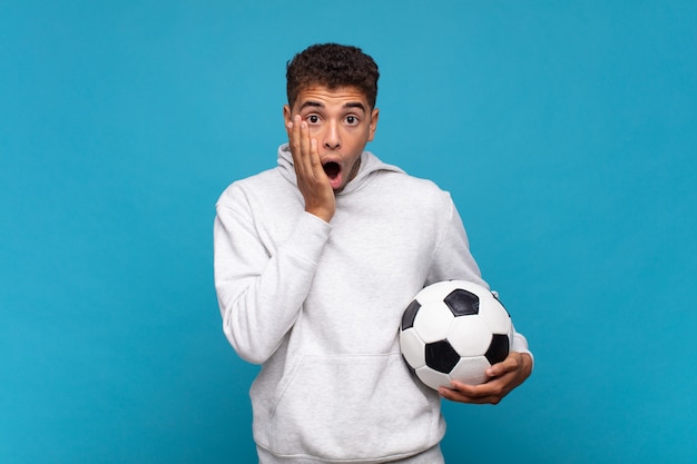 Young man feeling shocked and scared, looking terrified with\
open mouth and hands on cheeks. soccer concept