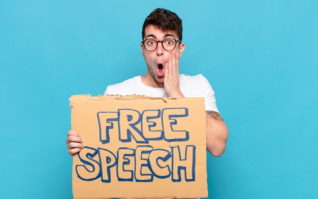 Young man feeling shocked and scared, looking terrified with open mouth and hands on cheeks