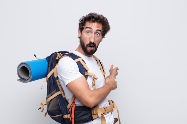 Young man feeling shocked and surprised, pointing to copy space on the side with amazed, open-mouthed look