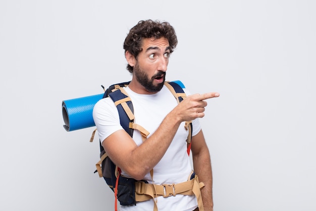 Young man feeling shocked and surprised, pointing and looking upwards in awe with amazed, open-mouthed look