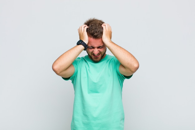 Young man feeling stressed and frustrated, raising hands to head, feeling tired, unhappy and with migraine