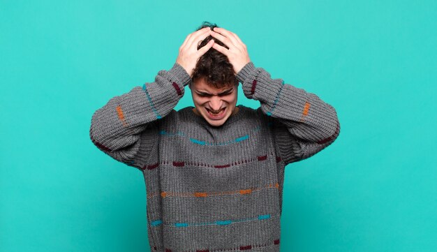 Young man feeling stressed and frustrated, raising hands to head, feeling tired, unhappy and with migraine