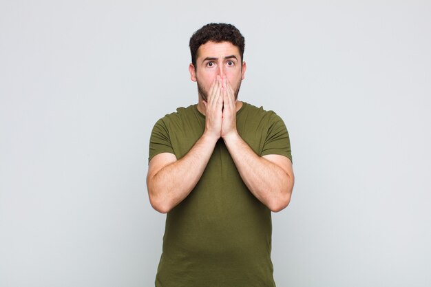 Young man feeling worried, upset and scared, covering mouth with hands, looking anxious and having messed up