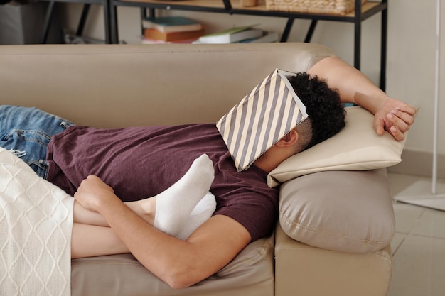 Young man fell asleep on sofa with opened book on his face