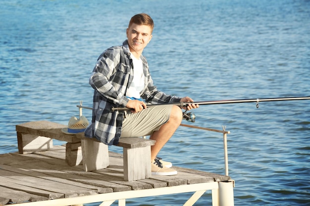 Young man fishing from pier on river