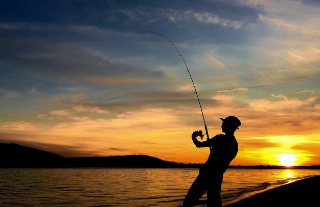 日没時に湖で釣りをする若い男