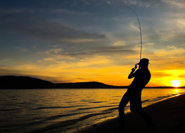 日没時に湖で釣りをする若い男