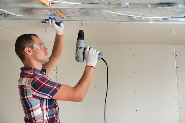 Young man in fixing drywall suspended ceiling