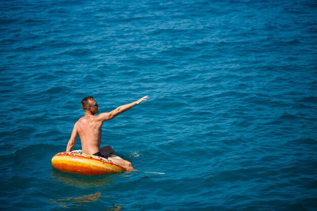 한 젊은이가 푸른 물이 있는 바다에서 팽창식 에어 링 원 위에 떠 있습니다. 행복한 화창한 날에 축제 휴가입니다. 휴가 개념, 상위 뷰입니다.