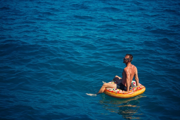 A young man floats on an inflatable air ring circle in the sea with blue water Festive holiday on a happy sunny day Vacation concept top view