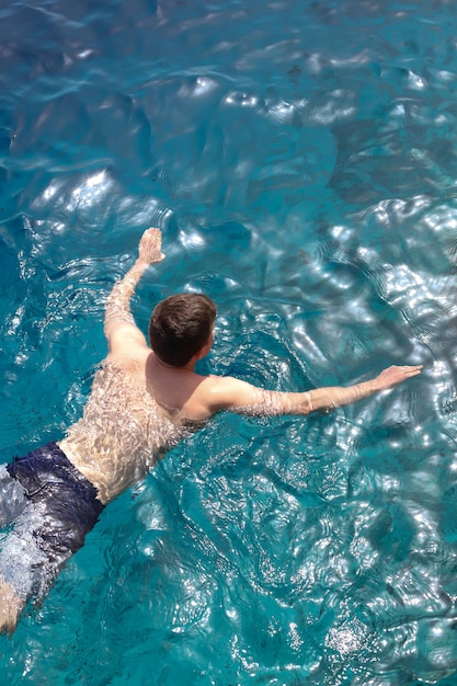 A young man floats on the sea, cutting through the blue water with his hands