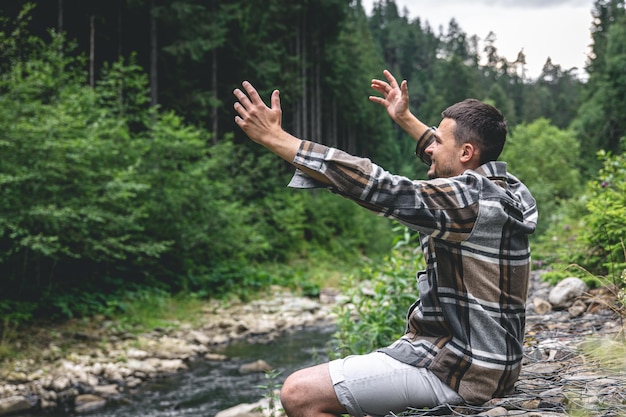 A young man in the forest near the river enjoys nature a halt