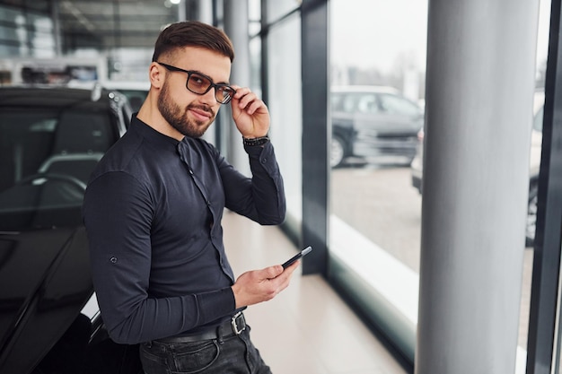 Young man in formal clothes is near brand new expensive car.