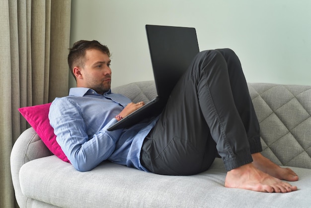 Young man freelancer working from home with his laptop laying on couch