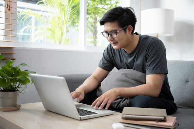 自宅のソファでコンピューターのラップトップで作業している若い男のフリーランサー。